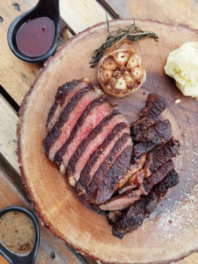 Ahşap bir tahtanın üzerinde orta pişmiş biftek, sos ve tuz.