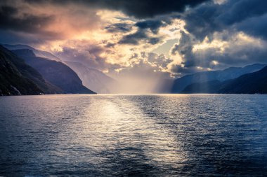 Norveç fiyordunda dramatik bir gökyüzü altında gün batımı