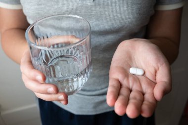 Hap ve bardak, elinde su olan bir çocuk. Eczaneden sağlık hizmeti. Çocuk hastalık yüzünden evde oturuyor..