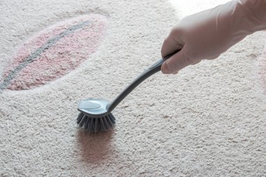 Beyaz kauçuk eldiven, yerde köpük beyazı halı ve temizlik için gri fırçayı tut.. 