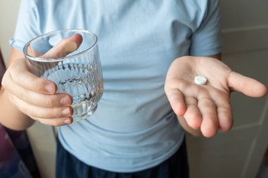 Elinde su olan beyaz hap ve bardak. Eczaneden sağlık hizmeti. Çocuk hastalık yüzünden evde oturuyor..