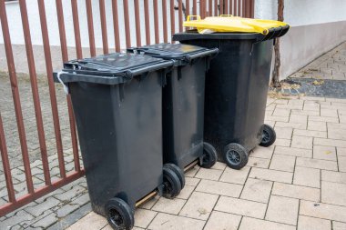 Sokaktaki sarı ve siyah çöp konteynırları. Yolun kenarındaki çöp yığını. Hijyen kavramı.