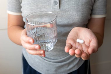 Hap ve bardak, elinde su olan bir çocuk. Eczaneden sağlık hizmeti. Çocuk hastalık yüzünden evde oturuyor..