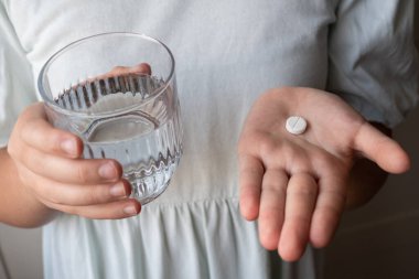 Hap ve bardak, elinde su olan bir çocuk. Eczaneden sağlık hizmeti. Çocuk hastalık yüzünden evde oturuyor..