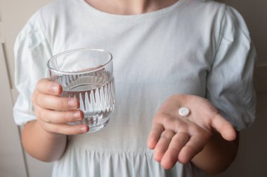 Hap ve bardak, elinde su olan bir çocuk. Eczaneden sağlık hizmeti. Çocuk hastalık yüzünden evde oturuyor..