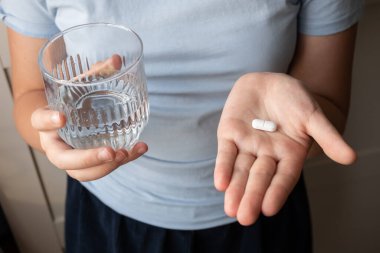 Hap ve bardak, elinde su olan bir çocuk. Eczaneden sağlık hizmeti. Çocuk hastalık yüzünden evde oturuyor..