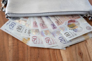 Ahşap arka planda İngiliz parası olan gümüş bir parti. Ticaret konsepti için deri cüzdanda United Kindom faturaları.