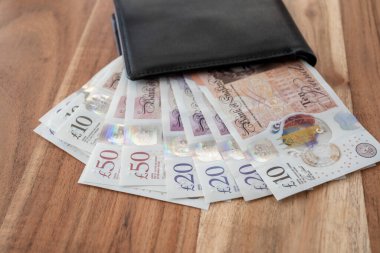 Ahşap masanın üzerinde İngiliz sterlini olan siyah deri bir parti. Ticaret konsepti için deri cüzdanda United Kindom faturaları.