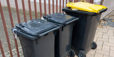 Sokaktaki sarı ve siyah çöp konteynırları. Yolun kenarındaki çöp yığını. Hijyen kavramı.