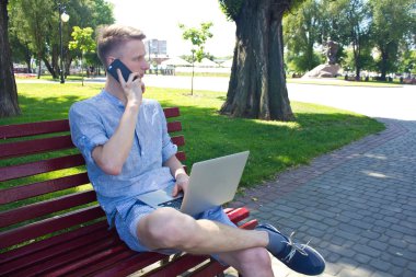 Dizüstü bilgisayar ile telefonda konuşan adam