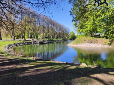 Slottsparken 'de büyük bir gölet, Malmö, yeşil ağaçlar ve taşlarla çevrili.