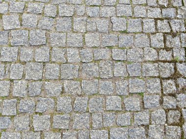 Eklemler arasında görünür yosun bulunan granit kaldırım taşı, düzensiz kare düzeni ve yıpranmış yüzey tarihi çağrıştırıyor