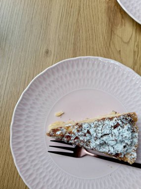 Pembe tabakta çatallı bir dilim kek, pudra şekeri vurgusu, sosyal içerik için genel kompozisyon, desenli ahşap