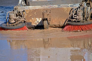 Bir sokak süpürgesinin fırçaları zaten sıvı olan çamuru bir sokaktan süpürüyor, bir hasarla üretiliyor, sağanak yağmurlardan sonra bölgeyi temizliyor, temizlik servisleri tarafından