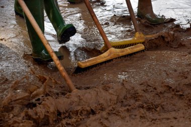 Yağmur botları ve fırçalar yerdeki çamur ve çamurla karışırken, zarardan etkilenen bölgeleri temizliyor.
