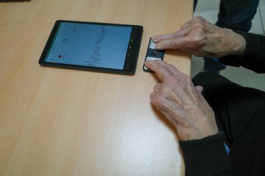 Doktor yaşlı bir kadının nabzını ölçer. Parmaklarını tablete koyar.