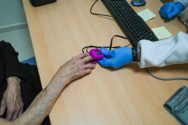 Rutin bir kontrol sırasında kan oksijeni monitörü kullanan yaşlı bir kadınla bir hemşire.