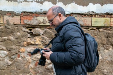 Elinde kamera olan bir adam, arka planda kırsal bir duvarla görüntülerin sonuçlarını görmek için ekrana bakar..
