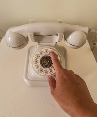 Beyaz bir masada altın aksanlı, klasik, beyaz bir telefon ahizesini tutan ya da çeviren bir el. Retro iletişimi ve nostaljiyi temsil ediyor. Yüksek kalite fotoğraf