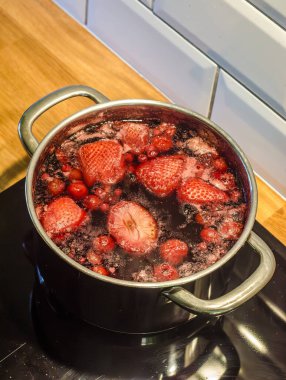 Ev yapımı yemek pişirme ve reçel hazırlama sırasında köpük, buhar ve zengin renkleri gösteren, fırında kaynayan karışık böğürtlenlerin canlı genel görüntüsü. - Evet. Yüksek kalite fotoğraf