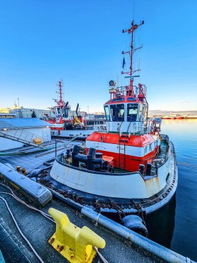 Limana yanaşan kırmızı ve beyaz römorkör endüstriyel iskele arka planı ve sakin yansıtıcı su ile. Deniz taşımacılığı, nakliye, lojistik ve deniz sanayisi. Yüksek kalite fotoğraf