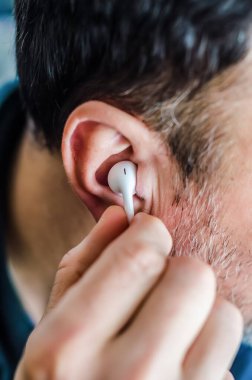 Kulağına beyaz bir kulaklık takan bir adamın yakın çekimi. Müzik, podcast, kişisel ses ve odaklanmış dinleme konsepti.