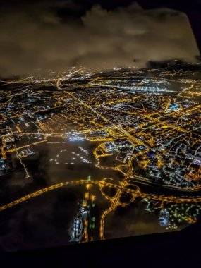 Geceleri genişleyen bir metropolün havadan bakış açısı. Bir uçak penceresinin manzarası, aşağıdaki aydınlık şehrin canlı enerjisini yakalar.