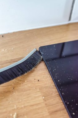 Ahşap tezgah ile siyah indüksiyon tenceresi arasındaki aralıktaki yiyecek kalıntılarını süpüren bir fırçanın yakın çekimi. Günlük mutfak temizliği ve ev işleri konsepti yüksek kaliteli fotoğraf.