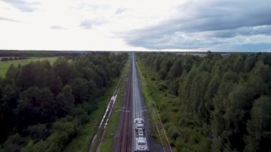 Modern yolcu treni elektrik hattı boyunca yeşil kırsal kesimde seyahat ediyor. Taşra manzarasında hareket eden trenin hava aracı görüntüsü, sakin seyahat havası, sürdürülebilir ulaşım, eko hareketlilik ve altyapı teması