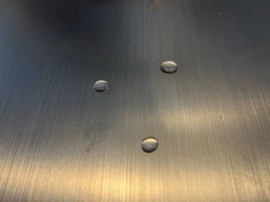 Fırçalanmış metal yüzeyde su damlacıkları