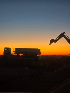 Dramatik günbatımı gökyüzüne karşı inşaat kazıcısının silueti. Sıkı çalışma, sanayi ve altyapı geliştirme kavramı.