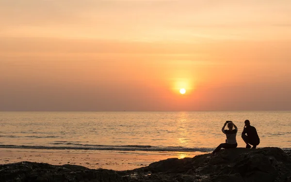 Seascape, silhueta casais sentados na rocha capturaram sua memória ao pôr do sol . — Fotografia de Stock