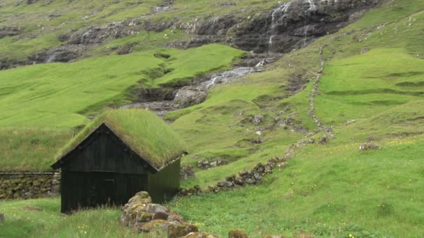 Casa con techo de hierba y cascada detrás en Saksun — Vídeo de stock