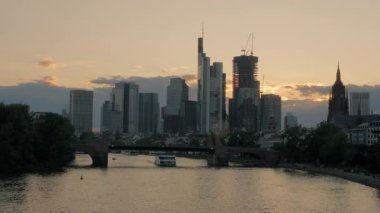 Frankfurt silueti ve River Main gün batımında Ignatz Bubis Köprüsü 'nden. Alte Köprüsü 'nün altından bir tur teknesi geçiyor