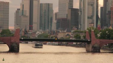 Alte Bridge Frankfurt 'un yakın klibi, tur teknesi altından geçerken. Frankfurt silueti arkada. Yaz akşamı çekilmiş.