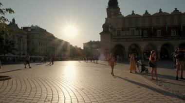 Krakow 'un ana meydanı Rynek Glowny' de günbatımında kamera yükseliyor. Meydanda bir sürü turist dolaşıyor.