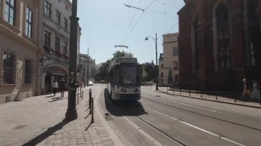 Kamera modern bir tramvayı Krakow Eski Şehir Polonya 'sındaki dar Dominikaska caddesinden geçerken izliyor.