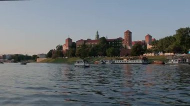 Bir yaz günü alacakaranlıkta Wawel Şatosu Krakow 'un düşük açılı geniş açılı klibi. Tur teknesi Vistula Nehri 'nin önünden geçiyor.