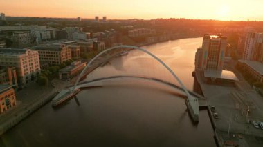 Drone, Newcastle Gateshead 'deki Millennium Köprüsü' nün etrafında güneş bir sonbahar sabahı doğarken izler sürüyor. Baltık merkezi arkada görülüyor.