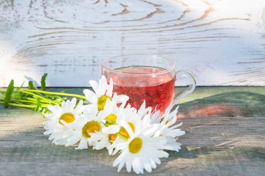 Bir demet beyaz papatya ve ahşap arka planda bir bardak cam çay.