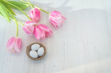 Mutlu Paskalya bayramı tebrik kartları. Pembe lale buketi ve beyaz ahşap arka planda beyaz yumurtaları olan kuş yuvası. Metin için boşluk