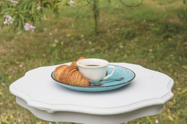Ay çörekleriyle kahvaltı ve yaz bahçesinde kahve. Beyaz kahve ya da çay, mavi tabakta sıcak kruvasan ve yaz bahçesinde klasik beyaz masa.