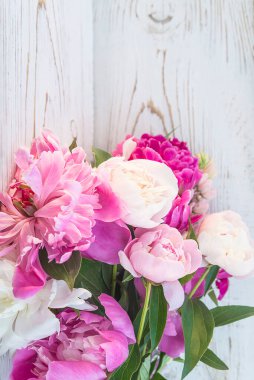 Beyaz boyalı ahşap arka planda pembe, beyaz ve mor şakayıklar.