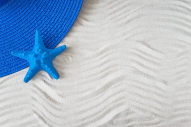 Yaz plajı tatili konsepti. Beyaz kum tepesinde kadın mavi şapkası ve mavi denizyıldızı, boşluğu kopyala