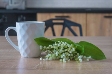 Beyaz fincan kahve ve vadideki ahşap masanın üzerindeki zambaklar.