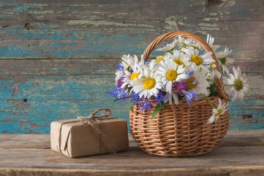 Yaz tebrik kartı; beyaz papatya buketi ve mavi çiçek ve eski ahşap arka planda el işi hediye kutusu