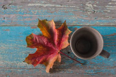 Boş kahve fincanı ve kırmızı akçaağaç yaprağı mavi boya eski ahşap arka plan