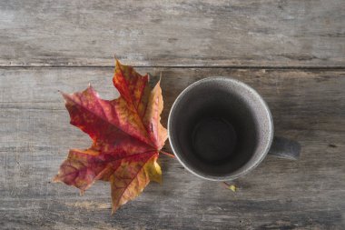 Boş kahve fincanı ve eski ahşap arka planda kırmızı akçaağaç yaprağı.; 