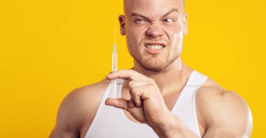 İlaç ve şırıngalı kaslı adamın stüdyo portresi, izole edilmiş sarı arka planda duran enjektör. Fitness, vücut geliştirme ve egzersiz konsepti