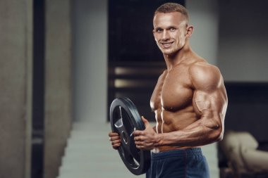 Beyaz tenli atletik adam kaslarını şişiriyor. Güçlü vücut geliştirici, karın kasları, trisepsleri, göğsü ve omuzları var. Fitness ve vücut geliştirme konsepti